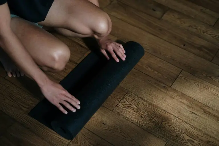 A man preparing for a yoga session by unrolling a black mat on wooden flooring in a yoga studio.