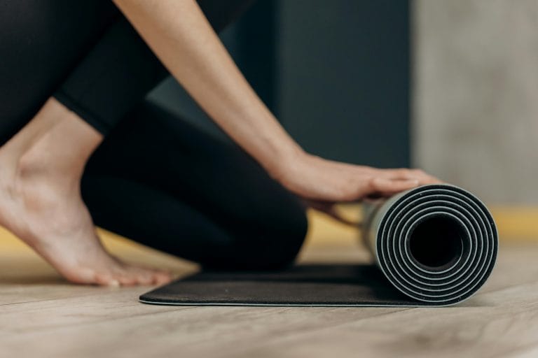 A young woman rolls up a yoga mat on a wooden floor, signifying tranquility and mindfulness.